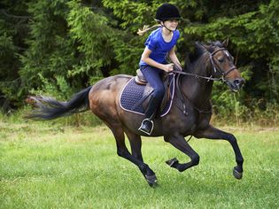 Side view of girl wearing riding hat galloping on horseback