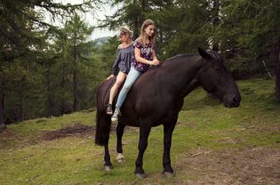 女孩和女人坐在马背上horse in a forest.