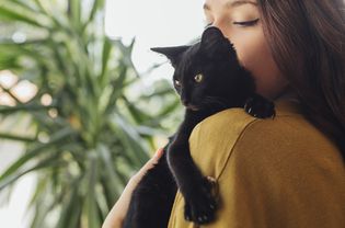 woman holds black cat on her shoulder