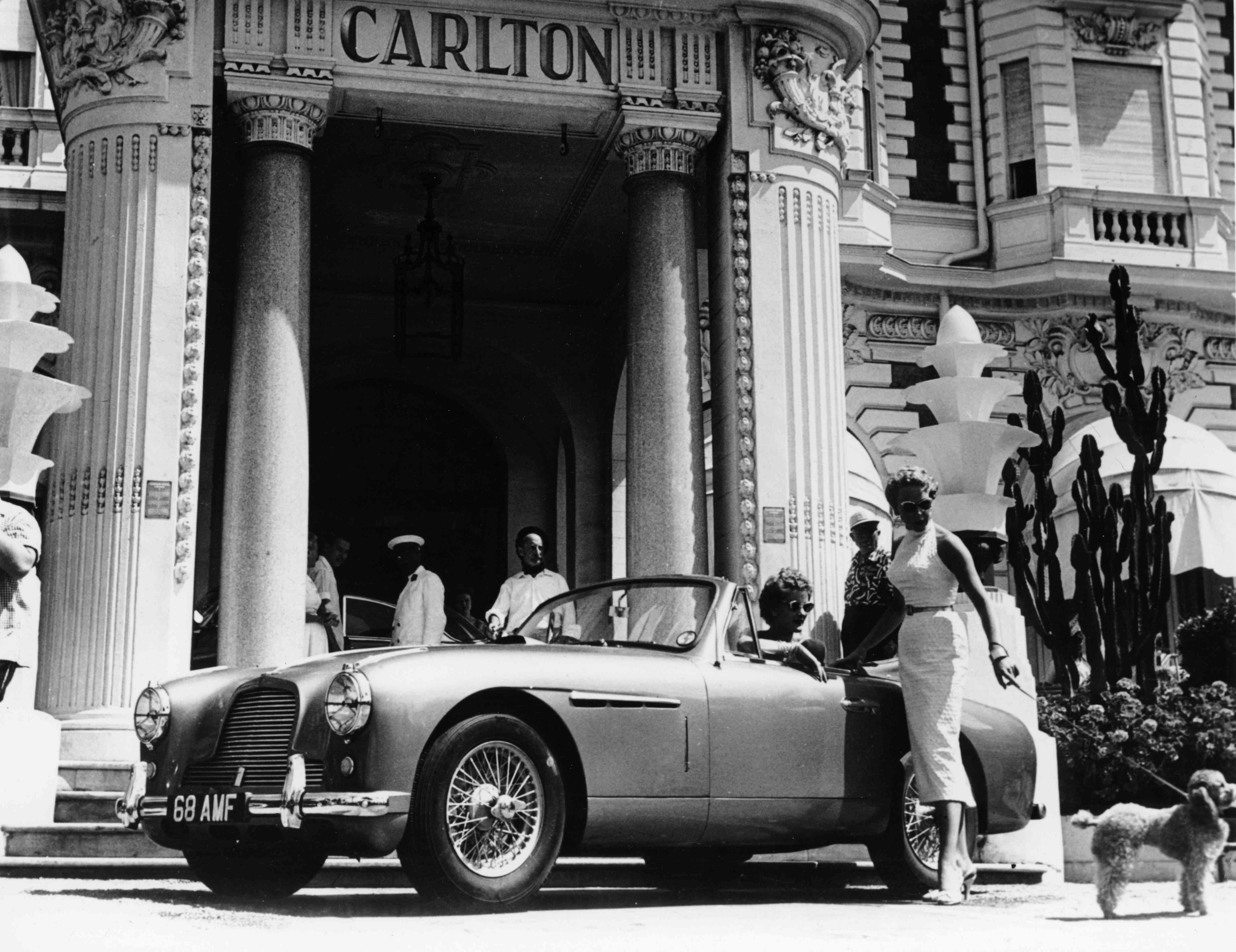 1955年，法国一家酒店外，一名妇女带着一只玩具贵宾犬靠近一辆汽车。