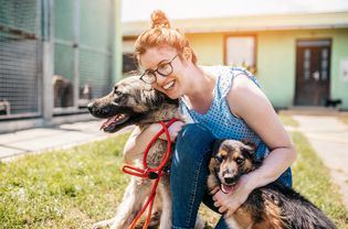 A volunteer hugs two dogs outside at a shelter