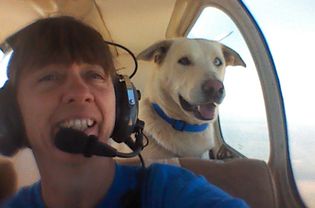 woman flying plane with white dog riding behind her