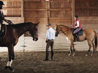 Young man standing between two riders and their horses in a training stable